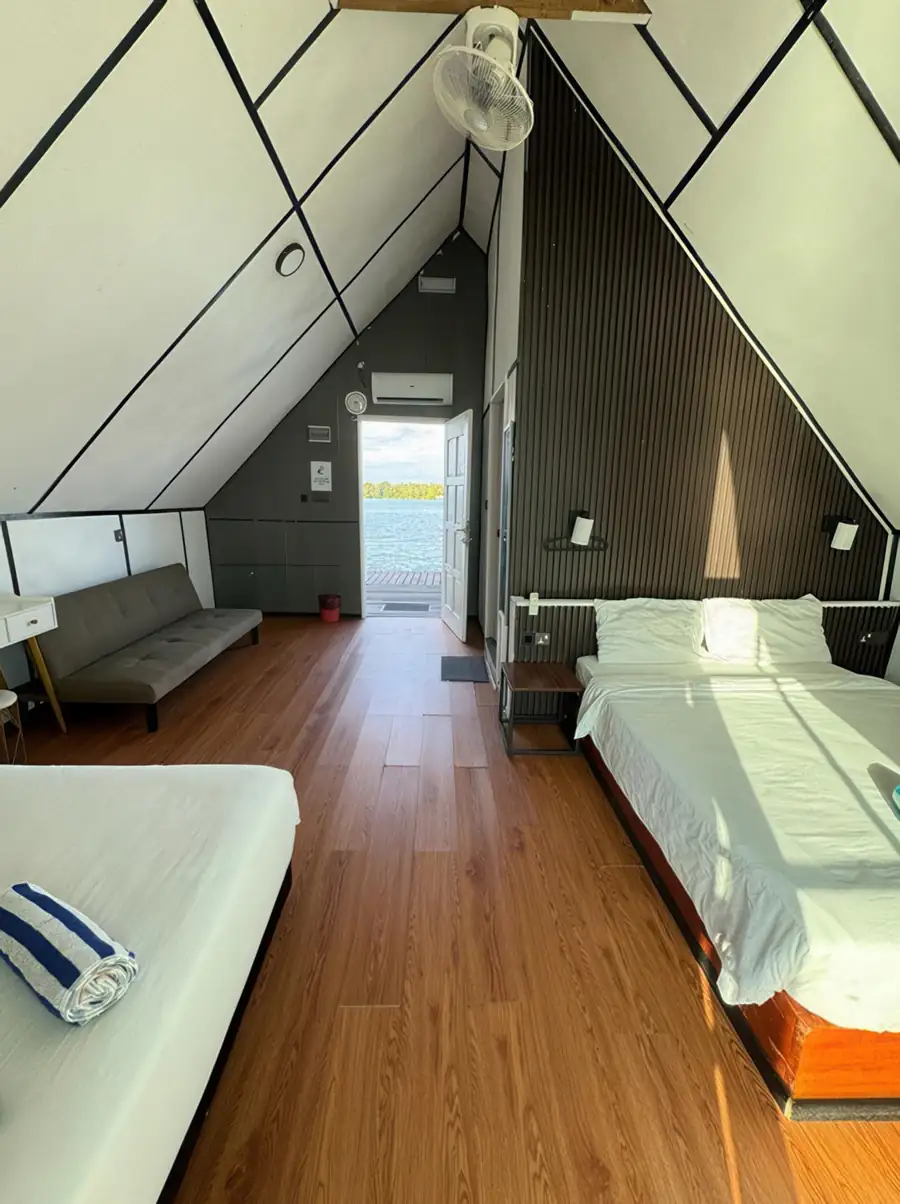 Double queen room at Adil Waterhouse Resort featuring two comfortable beds and an air conditioning unit while large windows invite the morning light inside near Pulau Bum Bum.