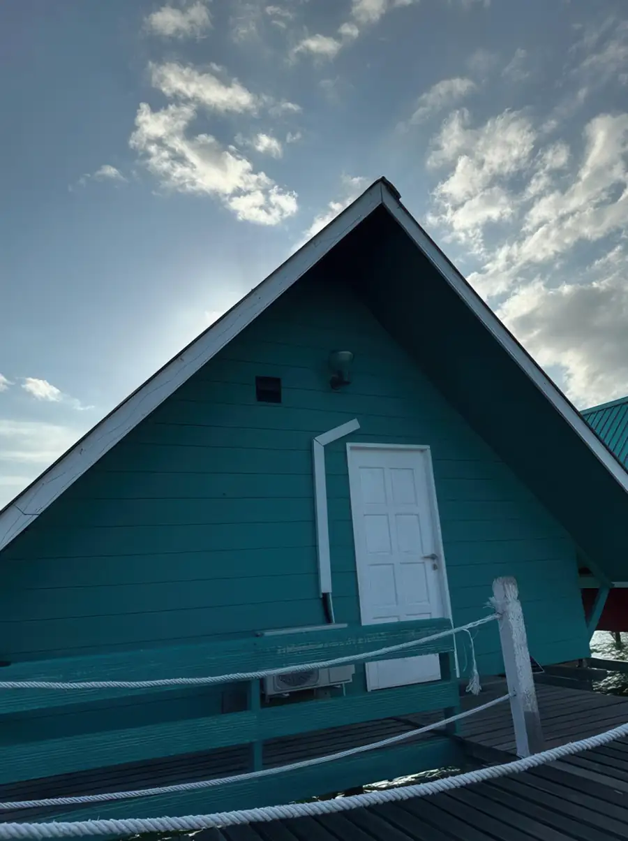 A close-up of a teal A-frame chalet showing the entrance door and deck railing at Adil Waterhouse Resort.