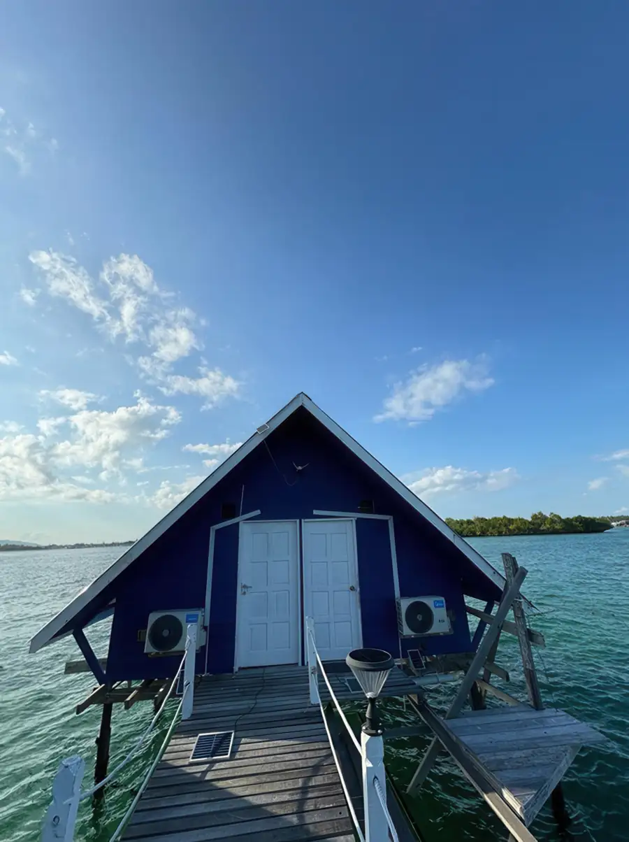 A blue A-frame water house standing over clear ocean waters at the end of a pier at Adil Waterhouse Resort.