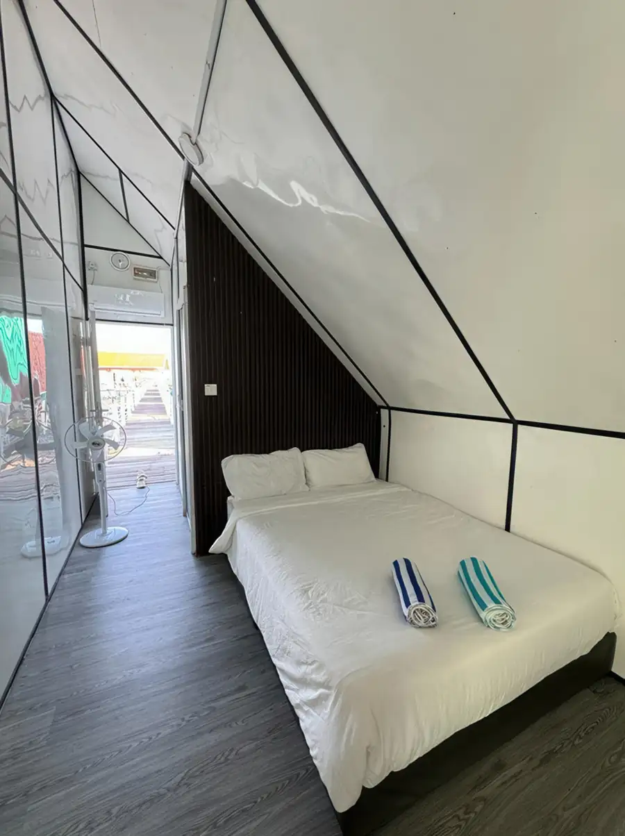 Queen room at Adil Waterhouse Resort featuring a large bed and an air conditioning unit with floor-to-ceiling glass doors that invite the tropical breeze inside over the Celebes Sea.