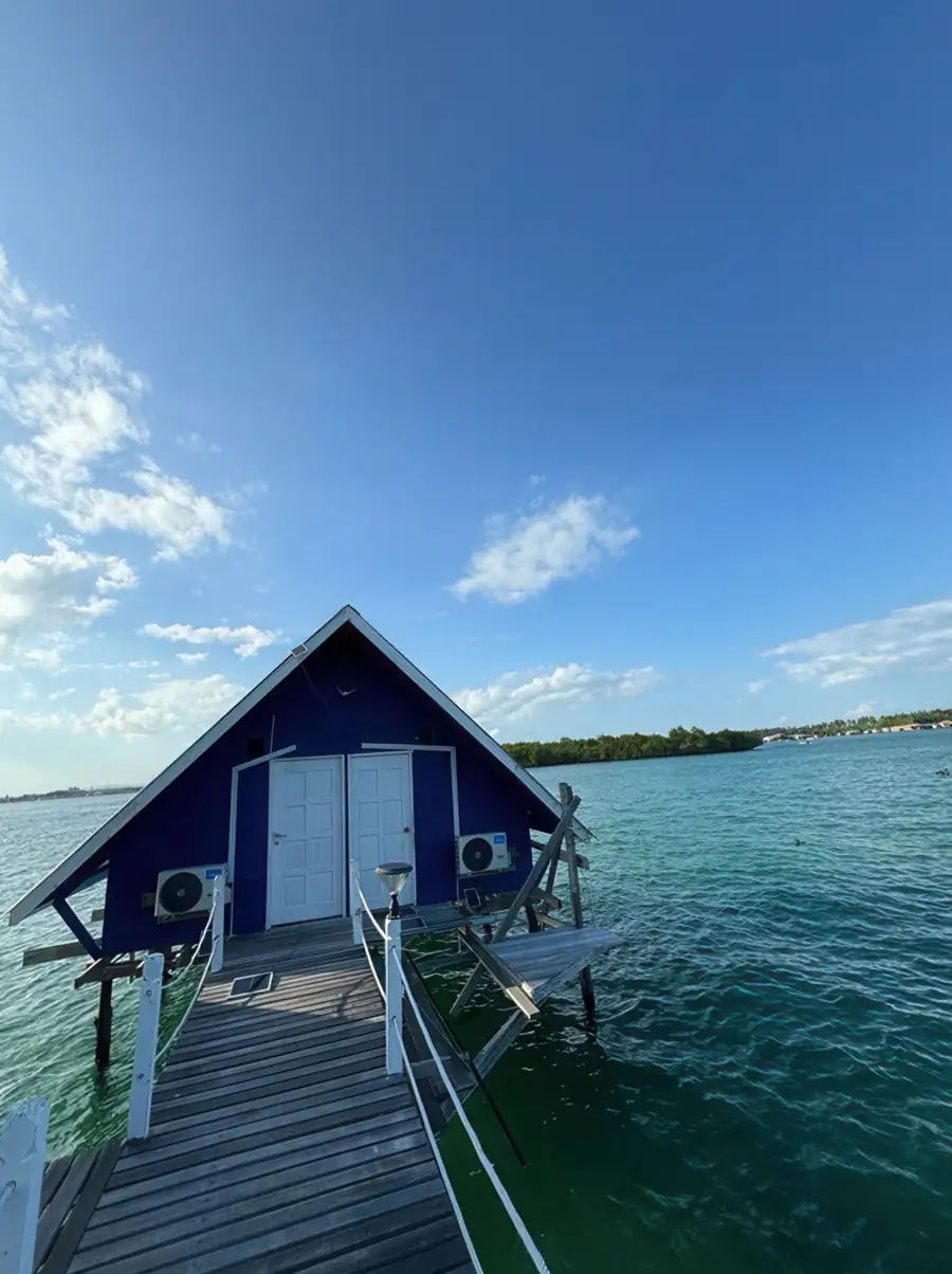 A secluded blue A-frame chalet over turquoise water at the end of a wooden walkway at Adil Waterhouse Resort.