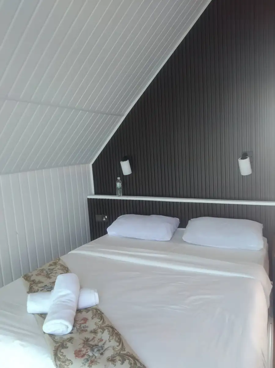 A unique bedroom at Adil Waterhouse Resort near Semporna featuring a large bed with floral accents, a wood-paneled feature wall, and a dramatic slanted white ceiling.